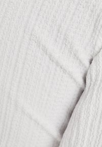 White textured fabric with a subtle wavy pattern. The weave appears soft with a slightly raised texture, creating visual depth and interest.