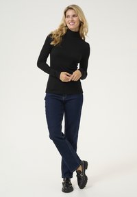 Juodas ilgomis rankovėmis turtlenecko stiliaus marškinėlis, derinamas su tamsiai mėlynomis tiesiomis kelnėmis ir juodais loafers, pasižymintis gliūti ir prisitaikančiu dizainu.