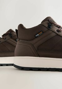 Braune Wanderschuhe mit einer strukturierten Oberschicht, ausgestattet mit einer leichten Sohle und einem ausgeprägten Profilmuster. Enthält Akzente aus Cordura-Gewebe.