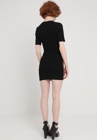 Svart ribbad miniklänning med korta ärmar, med en figurnära silhuett och färgglada sidostrikar. Svarta högklackade sandaler.