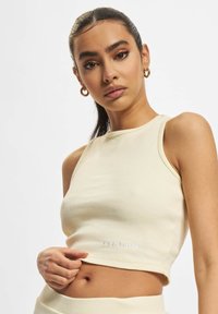 Lys beige ribbet crop top med et tett design, som har en rund halsutskjæring og subtil logo detalj ved kanten. Glatt tekstur.