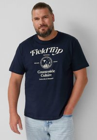 Navy blue t-shirt bawełniany z białym nadrukiem tekstu "Wycieczka" i okrągłą grafiką. Krótkie rękawy, luźny krój. Jasnoniebieskie dżinsy.