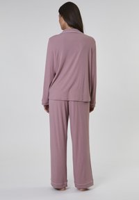 Ljusrosa pyjamakostym gjord av mjukt tyg, med lång ärm och vida byxor. Inkluderar en krage och diskreta kontrasterande detaljer.