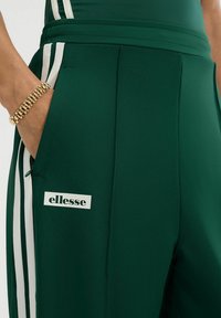 Groene atletische broek met witte zijstripes en een logo patch. Gemaakt van gladde stof met zakken en een gestructureerde tailleband.