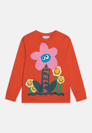 Red sweatshirt featuring a large pink flower with a blue face, green leaves, and smiling yellow flowers, with "STELLA" printed in black.
