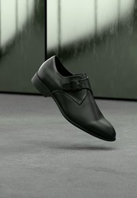 Μαύρο δερμάτινο παπούτσι με γυαλιστερό φινίρισμα, διακοσμημένο με μια όμορφη αγκράφα και κομψό σχεδιασμό. Ελαφρώς μυτερή μύτη και χαμηλό τακούνι.