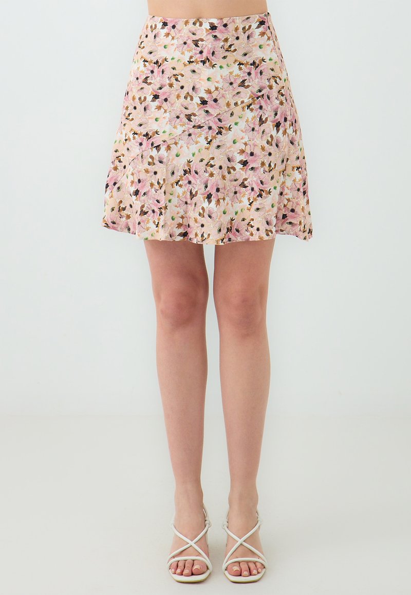 Floraler Minirock in zartem Rosa und Creme mit grünen Akzenten. Leichter Stoff, ausgestellte Form und dezenter Glanz. Kombiniert mit geschnürten weißen Sandalen.