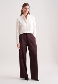 Witte blouse met lange mouwen en knoopsluiting, gecombineerd met bordeauxrode wijde broek. Getextureerde stof, getailleerde pasvorm en zwarte puntige hakken.