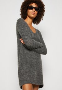 Vestido de suéter gris de punto con mangas largas y escote ancho; presenta un patrón texturizado de canalé y un corte relajado.