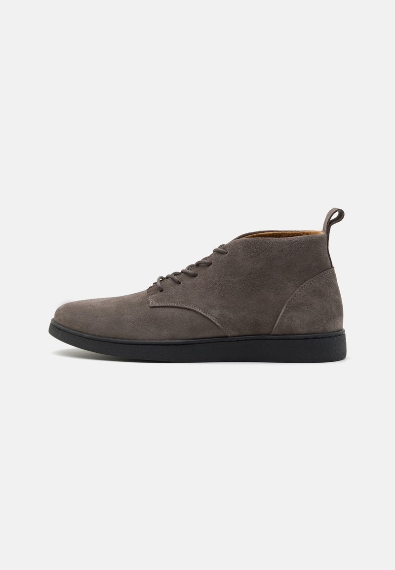Bottine en daim gris avec semelle noire, bout arrondi, lacets à l’avant et languette à l’arrière, vue de profil sur fond blanc.