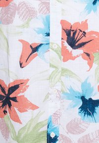 Nappapaita, jossa on kukkakuosi, jossa oransseja, sinisiä ja vihreitä kukkia valkoisella taustalla; kevyttä, teksturoitua kangasta.