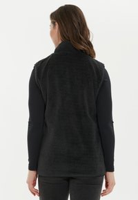 Musta, hihaton fleece-liivi, jossa on korkea kaulus ja pehmeä, teksturoitu kangas. Takana on suora helma eikä näkyviä kiinnityksiä.