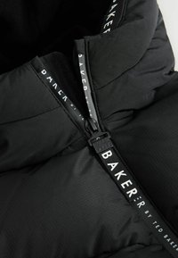 Intérieur d'une veste noire matelassée avec une fermeture éclair brillante et un tirant de marque. Texture douce et matelassée avec une doublure lisse et un détail de logo.