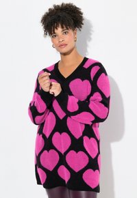 Schwarzer Oversized-Pullover mit V-Ausschnitt, der große rosa Herzmuster aufweist. Weicher Stoff mit langen Ärmeln und gerippten schwarzen Bündchen.