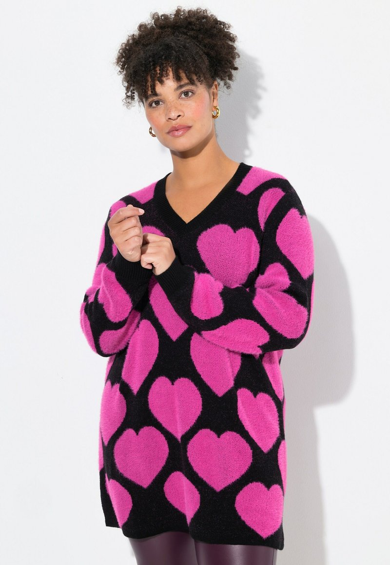 Schwarzer Oversized-Pullover mit V-Ausschnitt, der große rosa Herzmuster aufweist. Weicher Stoff mit langen Ärmeln und gerippten schwarzen Bündchen.