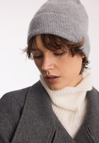 Szary prążkowany czapka, miękka mieszanka wełny, z zwężającą się górą; nałożona na kremowy sweter z golfem o teksturowanym splocie; ciemnoszary płaszcz.