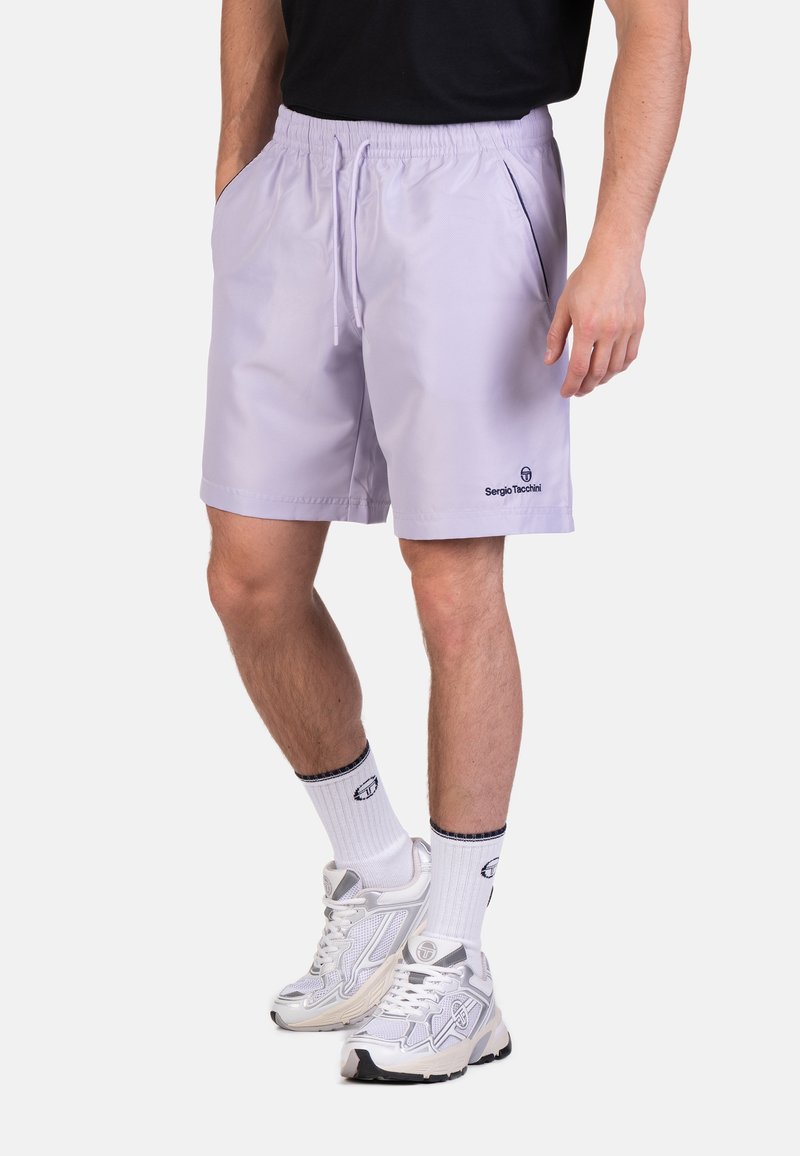 Shorts sportivi viola chiaro con vita elastica, tasche laterali e logo Sergio Tacchini sul lato sinistro in basso. Indossati con calze bianche e sneaker.