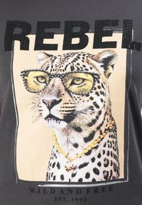 Leopard wearing studded sunglasses and a gold necklace with text "REBEL" above and "WILD AND FREE EST. 1995" below.