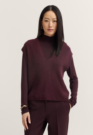 Burgunderfarbener Strickpullover mit V-Ausschnitt, kurzen Ärmeln und geripptem Muster. Kombiniert mit passenden Hosen für einen abgestimmten Look.