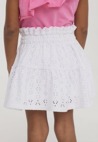 Gonna bianca in pizzo ad occhio di pernice con vita arricciata, design a strati e orlo ondulato, adatta per un abbigliamento estivo casual.