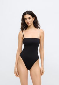 Μαύρο ολόσωμο μαγιό με ρυθμιζόμενους λεπτούς ιμάντες, τετράγωνο ντεκολτέ, ανοίγματα στα πόδια σε ψηλή κοπή και λεία, ελαστική υφή. Μινιμαλιστικός σχεδιασμός.