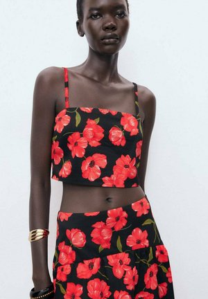 Black floral crop top featuring bright red poppies, thin straps, and a straight neckline, paired with a matching tiered floral skirt.