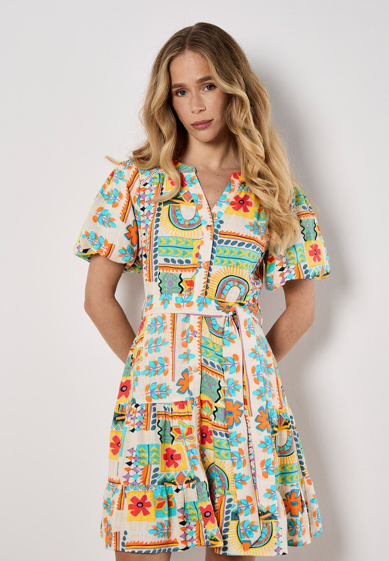 Robe colorée à motifs avec des manches courtes bouffantes, un décolleté en V et une taille cintrée, ornée de motifs floraux et géométriques sur un fond clair.