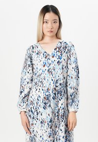 V-neck, long-sleeve dress in a lightweight fabric featuring a white base with a multicolored speckle pattern in blue, brown, and black.