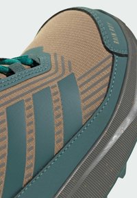 Brown textile sneaker with teal accents, featuring horizontal stripes, textured surface, and detailed stitching on the upper and sole.