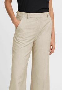 Beige, wide-leg trousers with a smooth texture, featuring side pockets and a tailored waistband. Paired with a black top.
