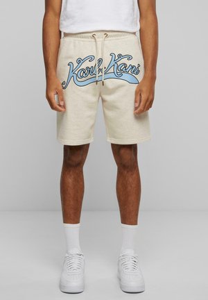 Beige cotton sweat shorts with an elastic waistband, drawstring closure, and a blue graphic logo on the front. Features side pockets.