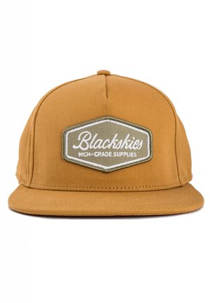 Geelbruine snapback pet met een platte rand en een gestructureerde afwerking. Voorzien van een hexagonaal patch met de tekst "Blackskies" in het wit.