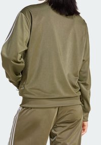 Olivově zelený sportovní komplet s lesklou texturou, obsahující kontrastní bílé boční pruhy na rukávech a nohavicích. Jednoduchý sportovní design.