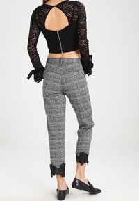 Top corto in pizzo nero con schiena scoperta; pantaloni grigi a quadri con rifinitura in pizzo nero all'orlo; modella che indossa ballerine nere.