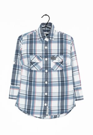 Camicia a quadri blu e bianca con accenti rossi, maniche lunghe, due tasche sul petto, orlo arrotondato e chiusura a bottoni. Il materiale sembra morbido e leggero.
