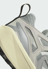 Light gray athletic shoe with mesh upper, silver accents, textured detailing, and beige rubber sole; features a black heel loop for easy wear.