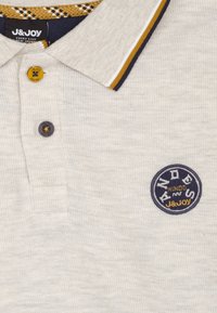 Polo shirt in lichtgrijs met ribbeltextuur, kraag met marineblauwe en gouden strepen, en een placket met twee knopen. Bevat een rond geborduurd logo in donkerblauw.