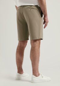 Shorts kaki cu croială dreaptă, talie ajustabilă, buzunare laterale și un buzunar posterior cu buton, asortați cu adidași albi.