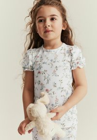 Koko pyjama kukallinen pehmeästä puuvillasta, jossa on vaaleansinisiä ja vaaleanpunaisia kukkia valkoisella taustalla. Puvussa on puffihihat ja aaltoileva kaula-aukko.