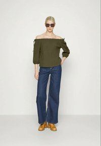 Top verde-azeitona, sem alças e com mangas bufantes e laços, combinado com jeans de perna larga azul-escuro e sapatos de salto bloco em tom beje.
