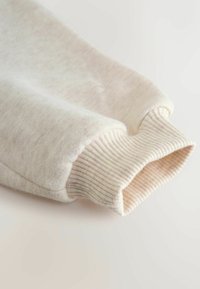 Ljusbeige sweatshirtärm tillverkad av mjuk, strukturerad tyg. Har ribbat manschett och en jämn, subtil färgvariation genom hela ärmen.
