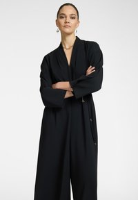 Mustat haalari pitkillä hihoilla, v-neck-muotoilu, rento istuvuus, valmistettu silkkisestä kankaasta. Sisältää hienovaraisia sivuaksentteja ja sidottavan vyötärön.