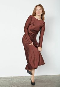 Ruda satino suknelė ilgomis rankovėmis su prigludusia palaidine ir laisva suknele. Audinys turi lygų paviršių, kurį papildo juodi aukšti kulniukai.