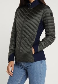 Mönstrad pufferjacka i mörkgrön med marinblå ärmar, med hög krage, full dragkedja och sidofickor för funktionalitet.