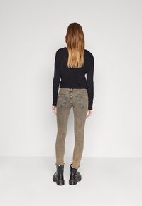 Suéter oscuro combinado con jeans skinny marrones descoloridos, con bajos desgastados y botas negras de tobillo con suelas gruesas. Diseño simple y ajustado.