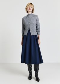 Grauer Strickcardigan mit hohem Kragen und vorderen Knöpfen, kombiniert mit einem marineblauen A-Linien-Rock und glänzenden schwarzen kniehohen Stiefeln.