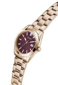 Reloj de pulsera tono dorado con un dial redondo, de color burdeos, marcadores de hora plateados y una pantalla de fecha; cuenta con una pulsera de acero inoxidable.