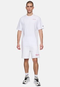 Hvid bomuld t-shirt med korte ærmer og et rødt broderet logo på brystet, parret med hvide shorts med "R.S.V.P." i rødt.