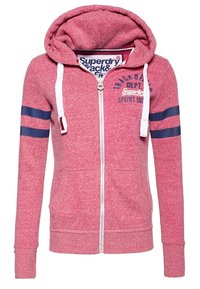 Felpa rossa con zip e lacci bianchi, righe doppie blu sulle maniche, tasche frontali e testo "Superdry Track & Field" sul petto.