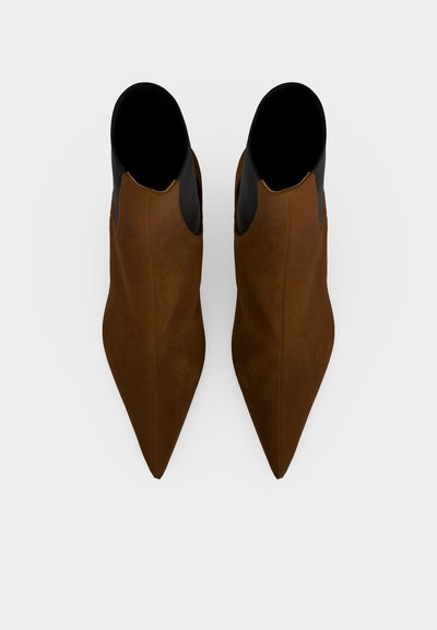 Paire de bottines marron à bout pointu avec des panneaux latéraux élastiques noirs, vues de dessus sur un fond clair.